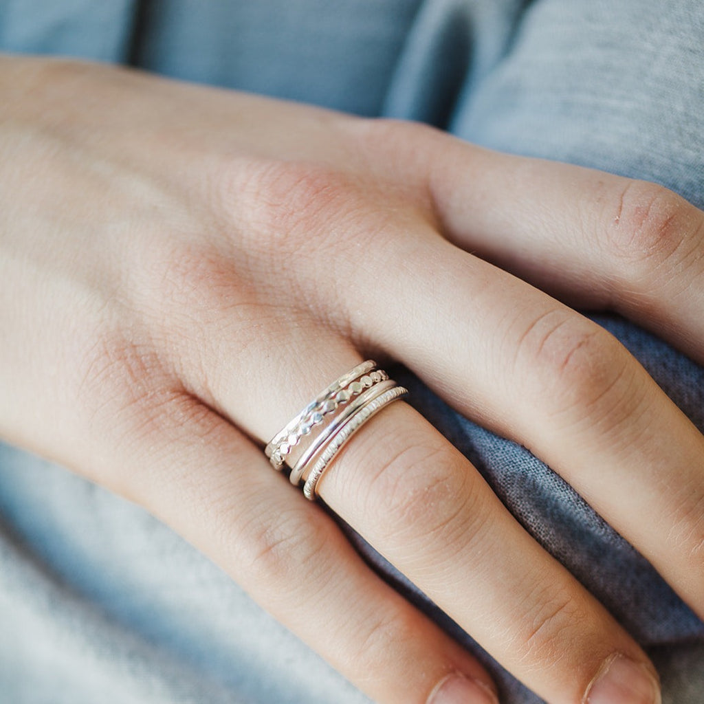 Woman wearing a stack of four sterling silver rings in four different textures.  A hammered ring, beaded ring, birch ring, and a smooth ring