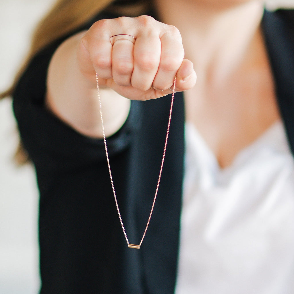 Woman holding minimalist handmade 14k solid gold chain with bar pendant