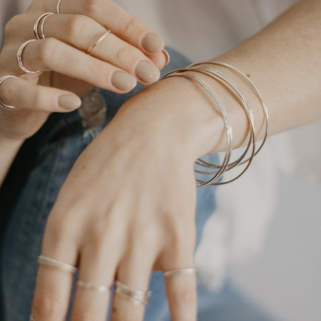 Woman wearing minimalist handmade sterling silver stacking bangles and rings