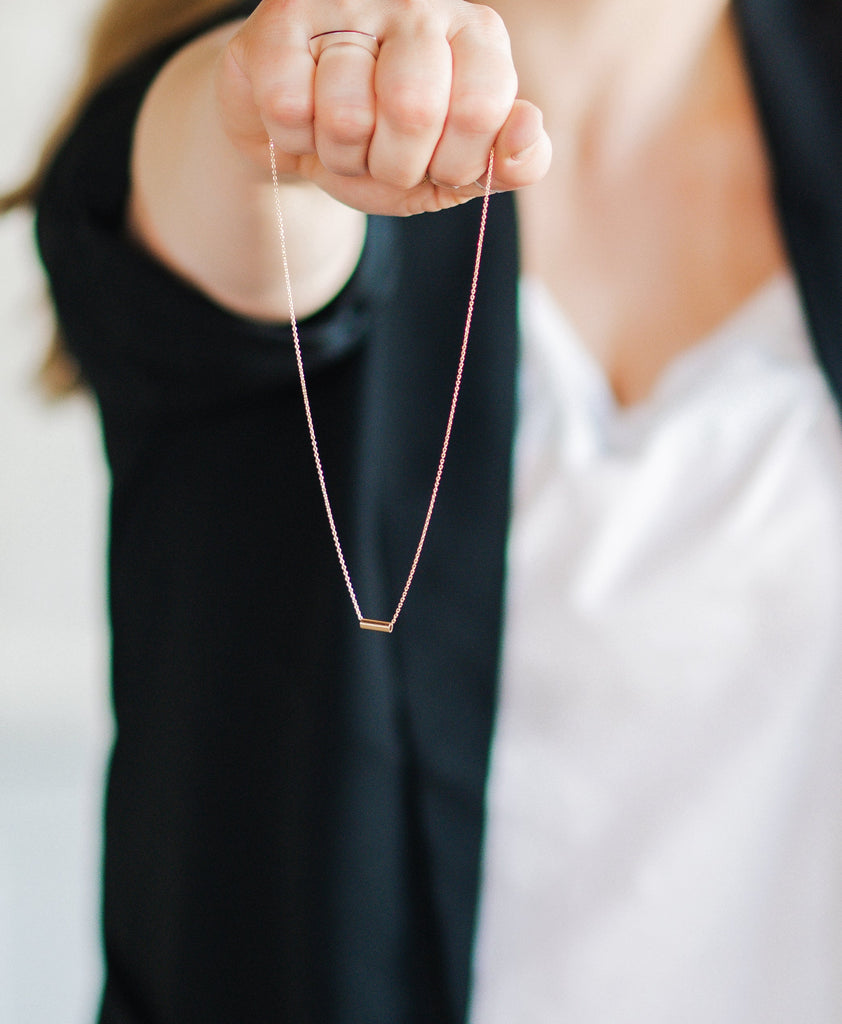 Woman holding minimalist 14k solid gold adjustable chain with bar pendant