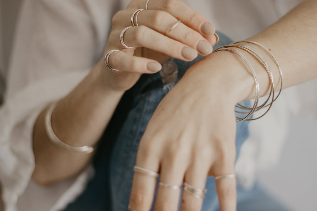 Woman wearing minimalist handmade sterling silver and 14k solid gold stacking rings and banglesi