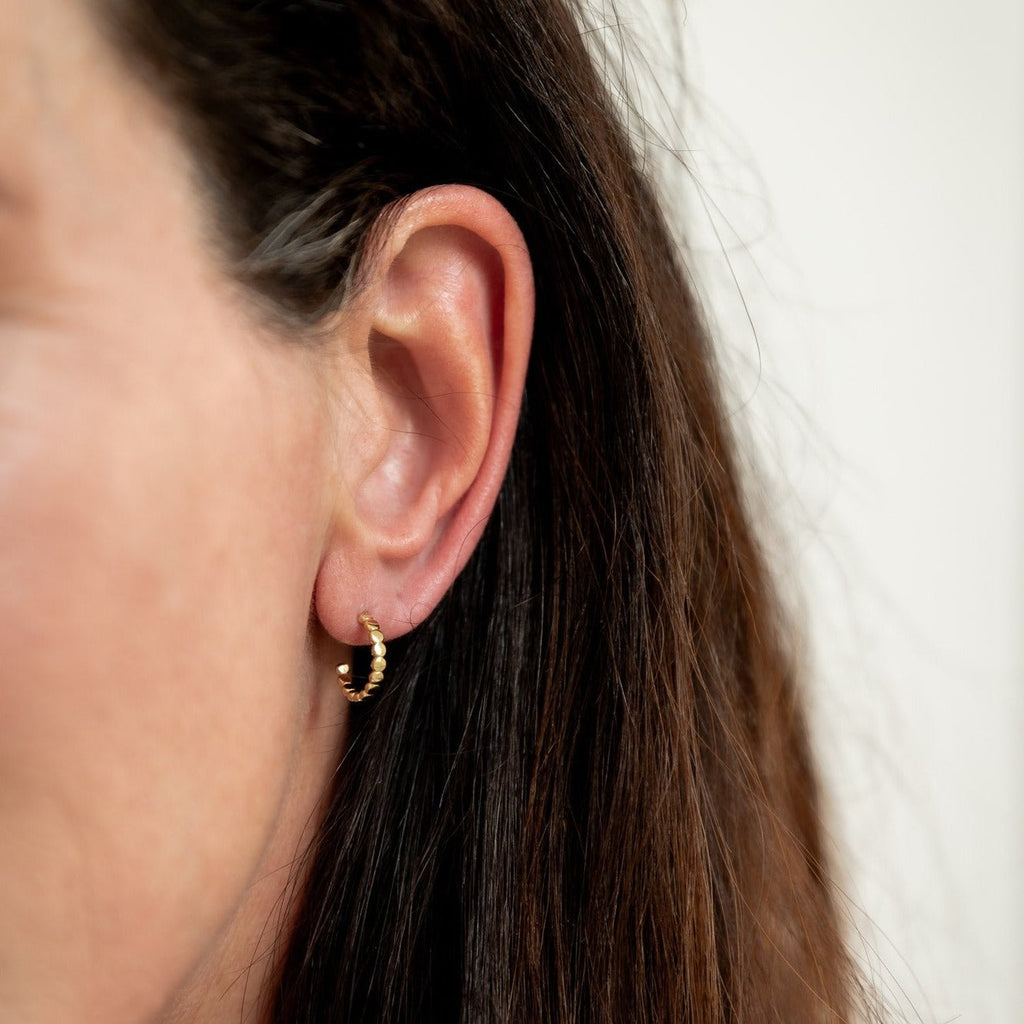 Woman wearing solid 14k gold beaded mini hoop earring 