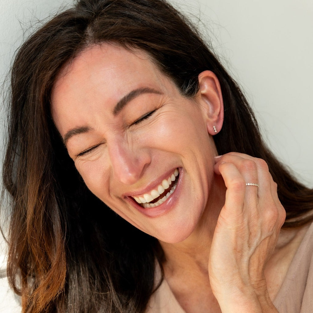 Woman laughing and wearing sterling silver stud earrings as well as a sterling silver beaded ring