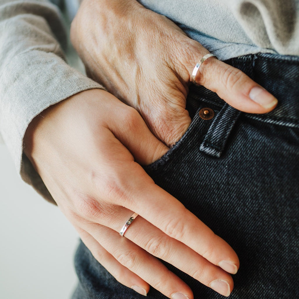Two hands in one jeans pocket, one hand from a mother and one hand from a daughter.  Each had wearing a 2.5mm wide band silver ring with a hammered finish.