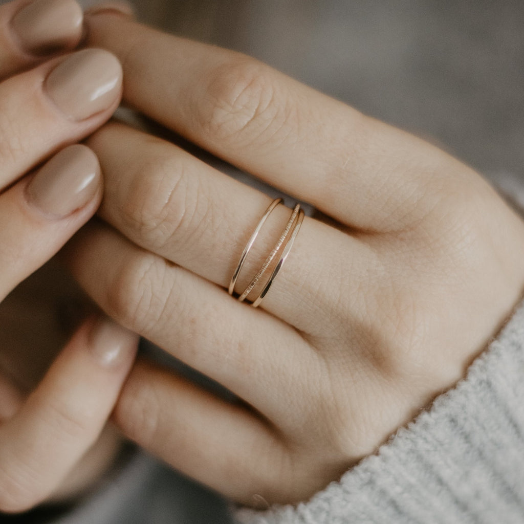 Hands wearing minimalist handmade 14k solid gold stacking rings with in a smooth birch and faceted texture