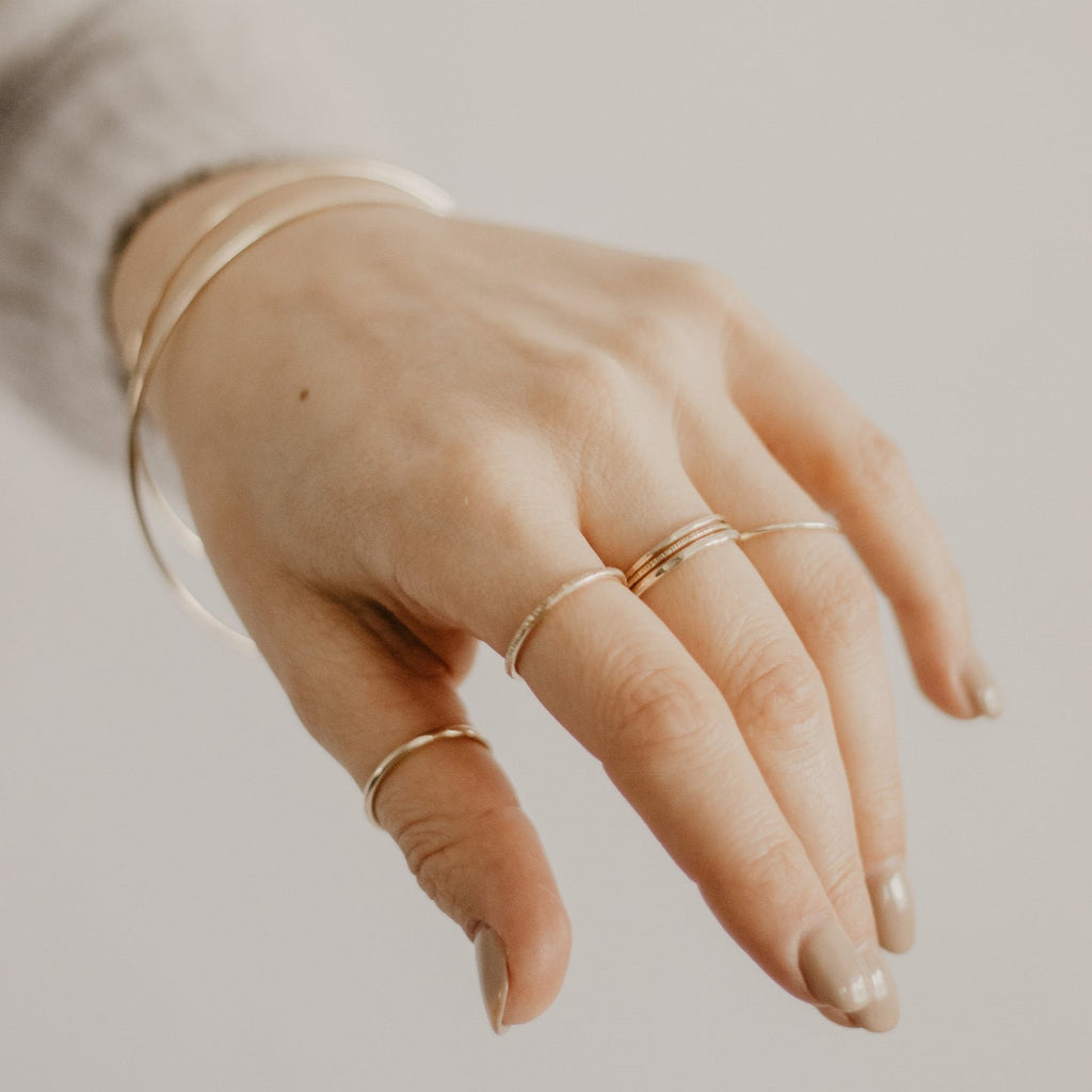 Hand with multiple minimalist handmade 14K solid gold stacking rings and bangles